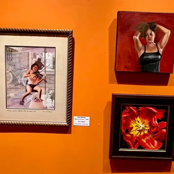 Three framed artworks on an orange wall: a violinist, a woman, and a red flower.