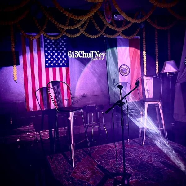 A stage with American and Indian flags, 615chuTNey banner, chairs, microphone, and purple lighting.