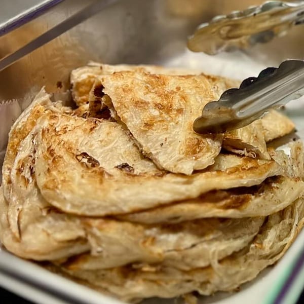 Close-up of golden-brown Indian paratha flatbreads in a serving dish with tongs.
