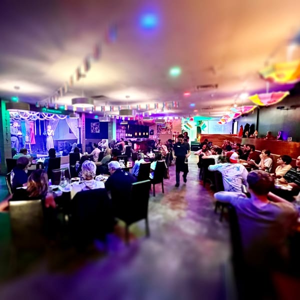 A lively Indian restaurant interior with a stage, performers, and diners enjoying the vibrant atmosphere.