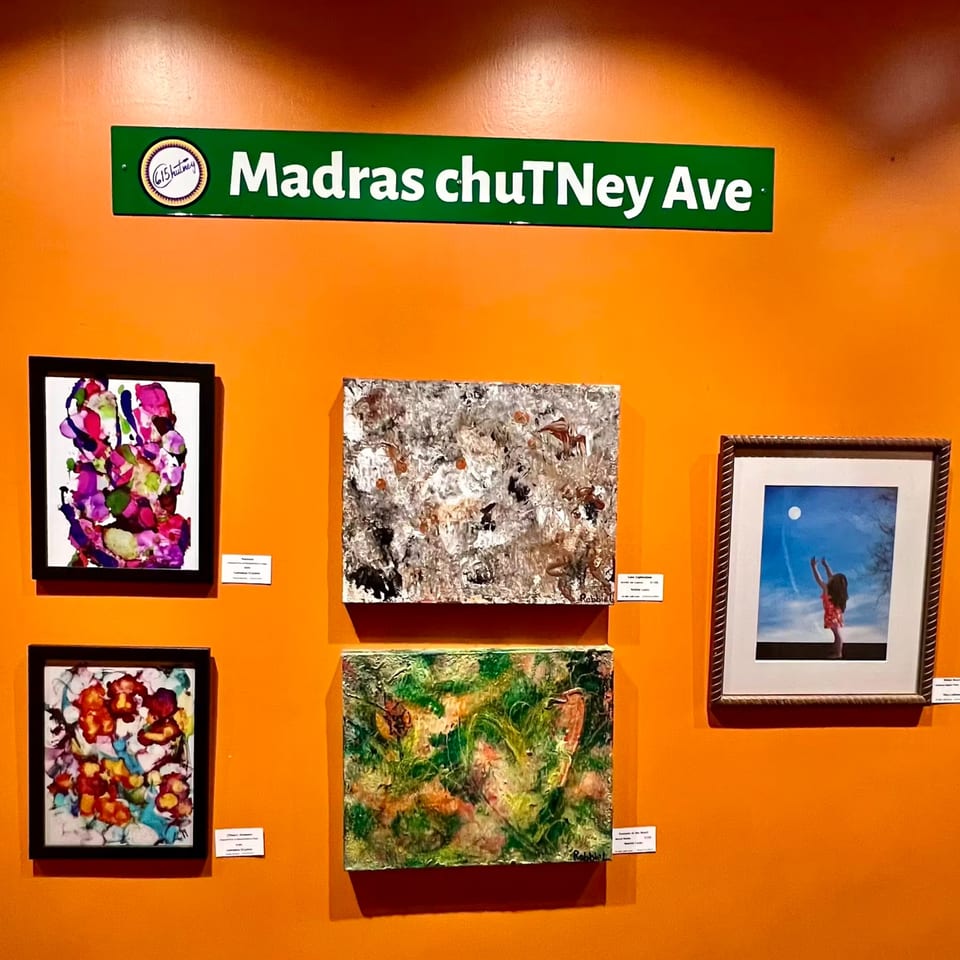 A green "Madras chuTney Ave" sign above five colorful abstract paintings on an orange wall.
