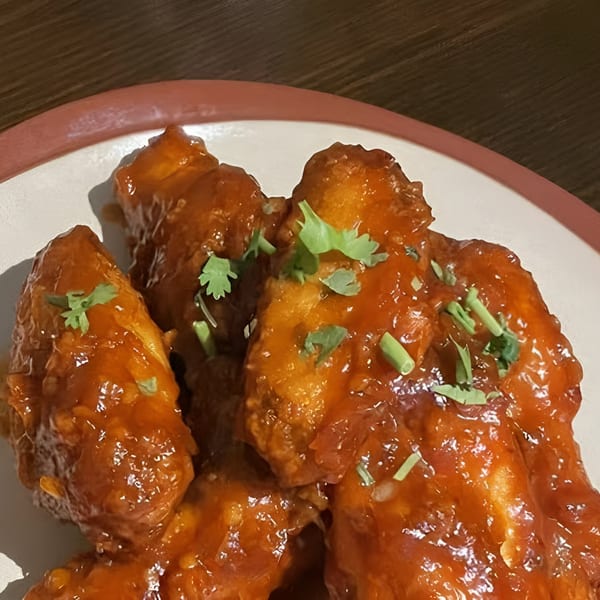 Close-up of Indian-style chicken wings coated in a glossy, reddish-orange sauce and garnished with cilantro.