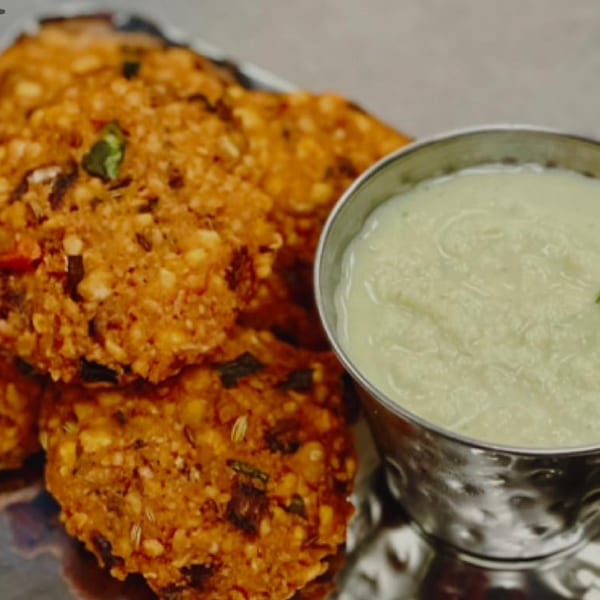 Crispy Indian lentil fritters (vada) with a side of creamy coconut chutney on a silver platter.