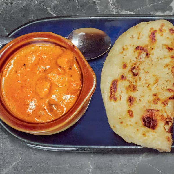 A bowl of orange Indian curry with a spoon and a piece of naan bread on a blue plate.
