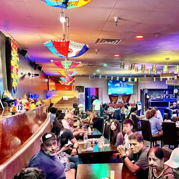 A vibrant Indian restaurant interior with colorful umbrellas, flags, and diverse patrons dining.
