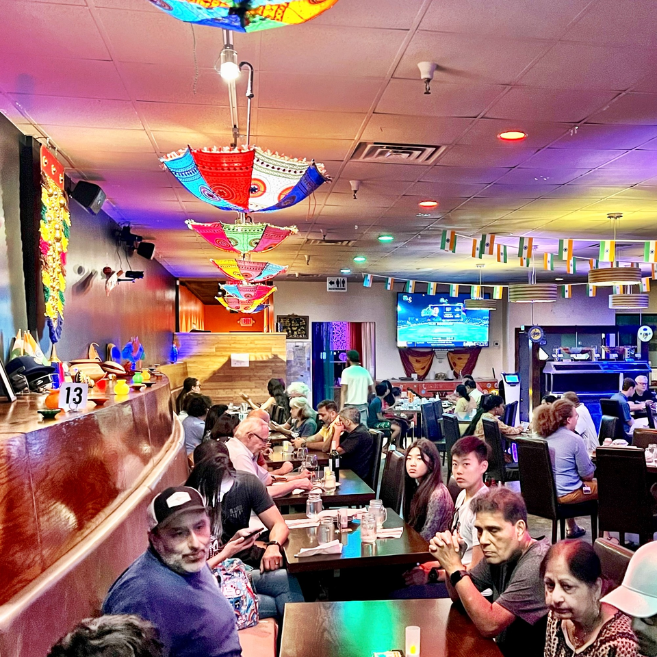 A vibrant Indian restaurant interior with colorful umbrellas, flags, and diverse patrons dining.