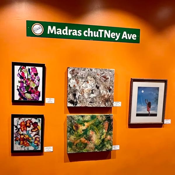 A green "Madras chuTney Ave" sign above five colorful abstract paintings on an orange wall.