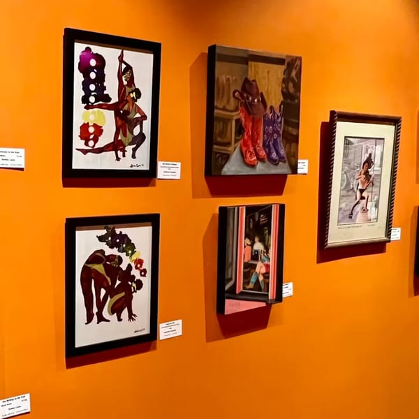 Various framed artworks, including abstract figures and cowboy boots, displayed on a vibrant orange wall.