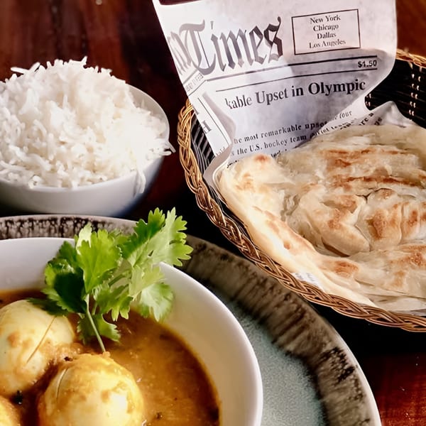 Indian egg curry with cilantro, white rice, and paratha bread in a basket with a newspaper.