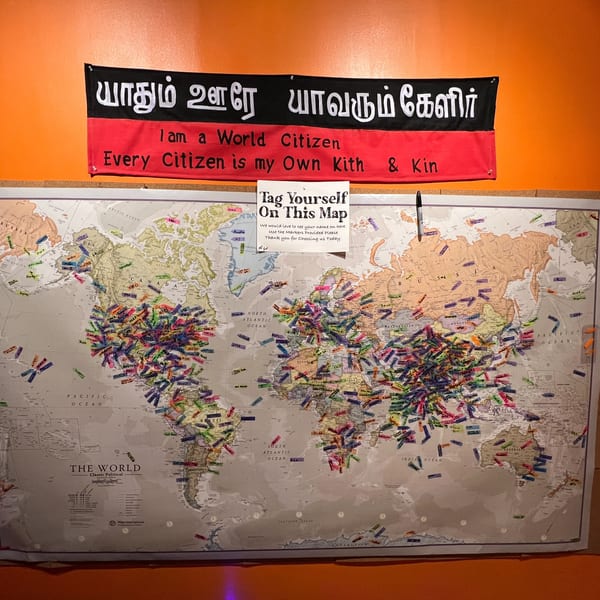 A world map covered in colorful sticky notes with names, below a banner with Tamil script and English translation.