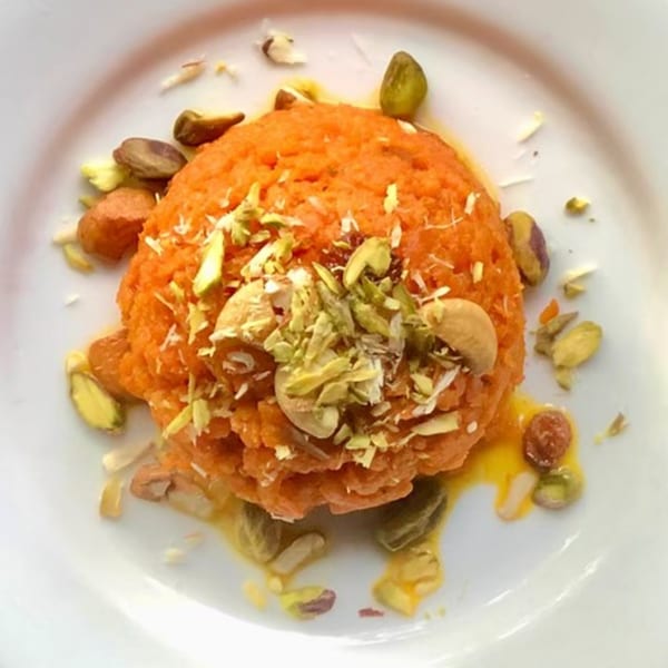 Indian Gajar Halwa dessert, an orange carrot pudding, topped with cashews and pistachios on a white plate.