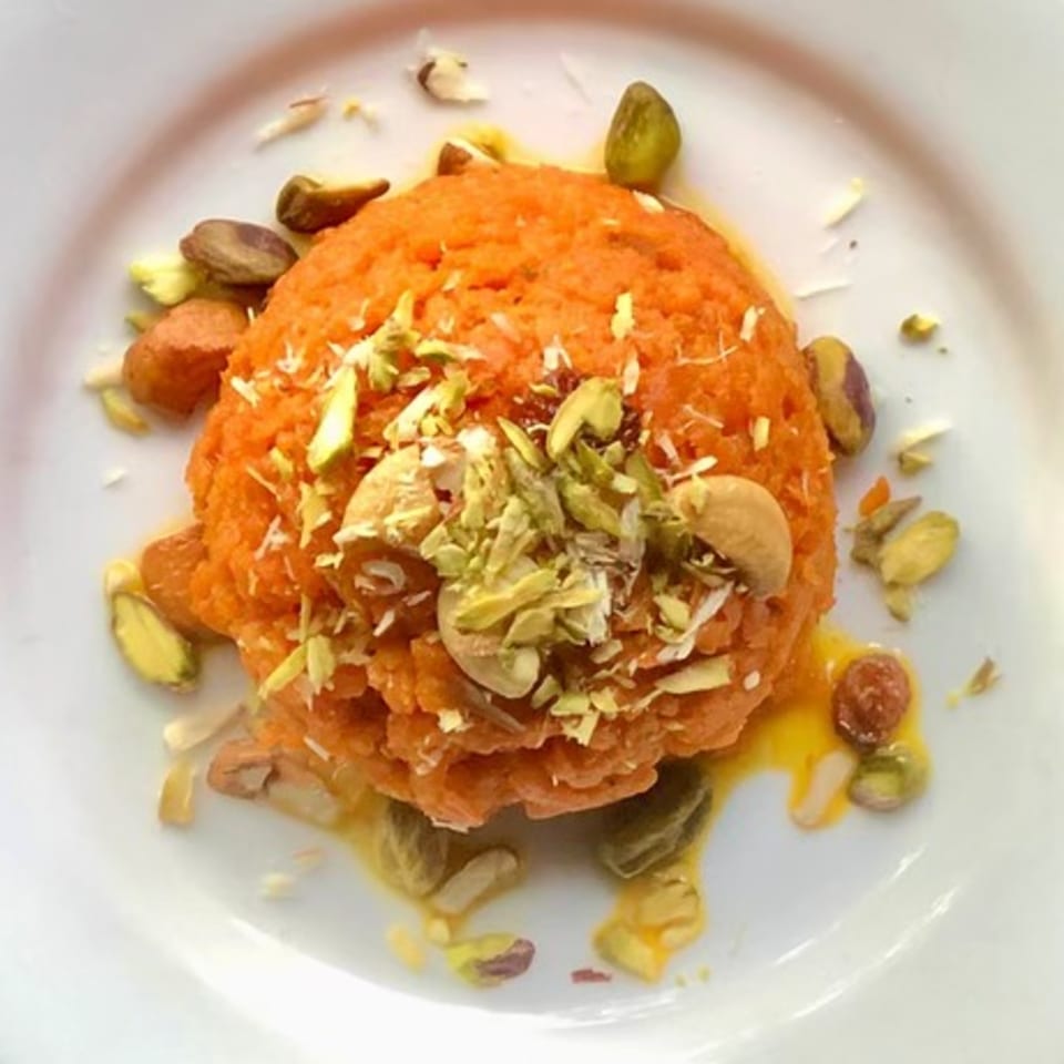 Indian Gajar Halwa dessert, an orange carrot pudding, topped with cashews and pistachios on a white plate.